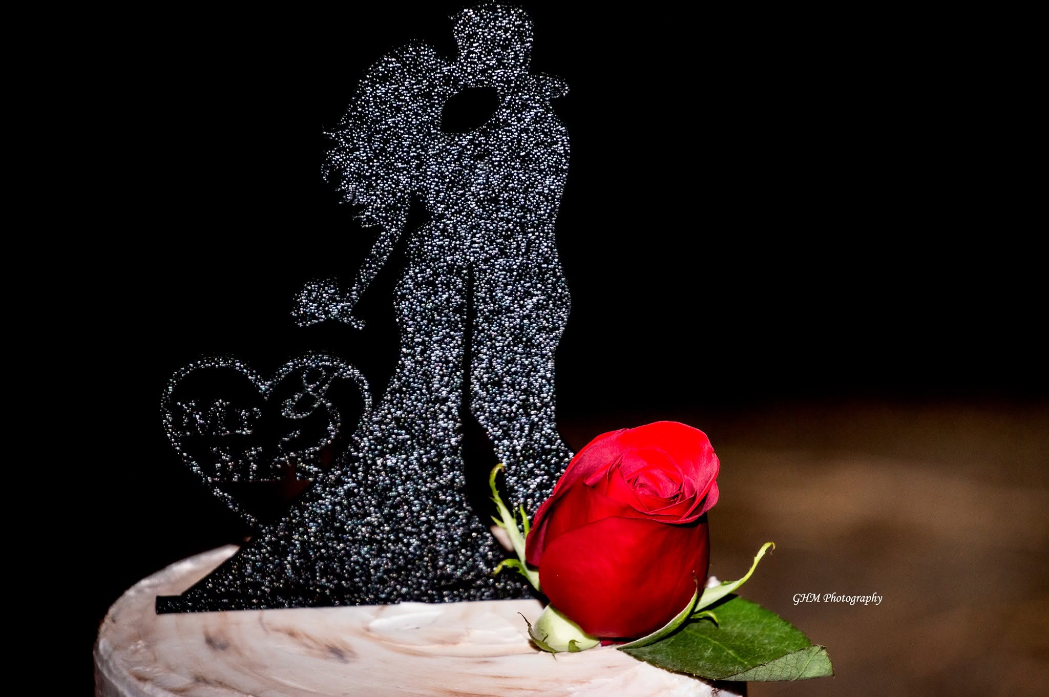 A couple cake topper beside a vivid red rose